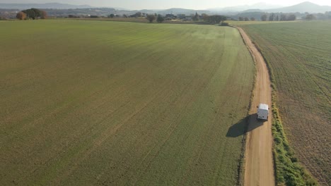 Aerial-video-of-a-newly-seeded-field-with-a-dirt-road-in-the-middle-and-mountains-in-the-background-green-Llagostera-Gerona-cultivated-field-Chasing-a-white-van