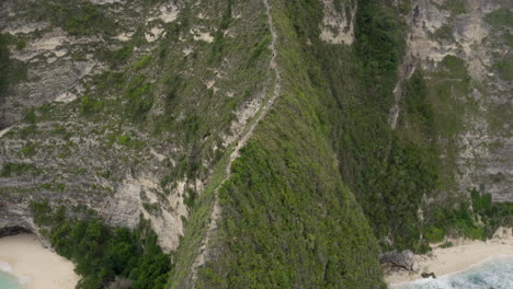 Fly-by-along-the-ridge-with-a-pathway-down-to-Kelingking-Beach-next-to-huge-steep-cliff,-Nusa-Penida,-Bali,-Indonesia