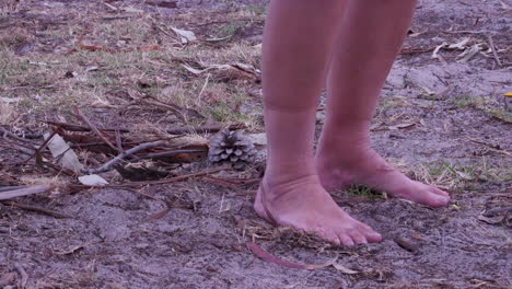 A-person-walking-barefoot-through-dirt-past-two-pine-cones