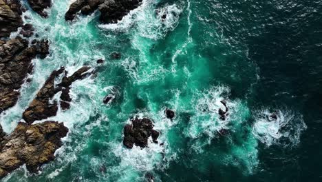 Top-down-view-of-deep-blue-waves-crashing-on-brown-rocks,-Slow-motion,-Big-Sur-California