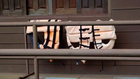 An-establishing-shot-of-three-old-orange-faded-lifejackets-hanging-over-the-railing-of-a-houseboat-drying-in-Kanchanaburi,-Thailand