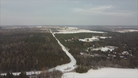Aerial-Shot-Of-A-Car-Driving-On-A-Snow-Covered-Road-Surrounded-By-Forest-In-Winter