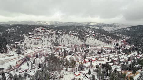 Drone-Aerial-View-Of-Snow-Covered-Winterscape-Town-In-Pine-Tree-Hill-Mountainrange-Valley