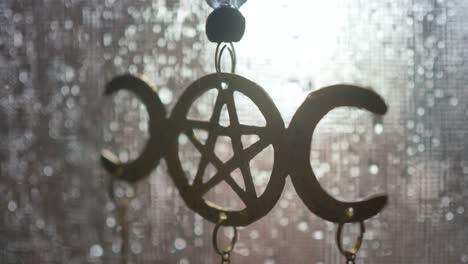 Close-up-of-a-moon-pentagram-decoration-hanging-in-a-screen-window-on-a-rainy-day