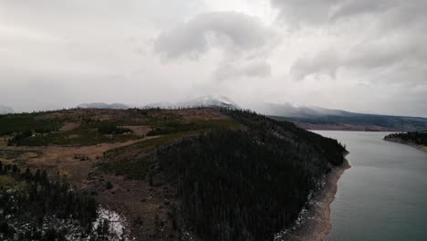 Cloudy-Moody-Drone-Aerial-View-Flying-Over-Lakeside-Pine-Tree-Hill-Revealing-Body-Of-Water-Sapphire-Point-Dillon-Reservoir,-Colorado