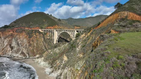 Aerial-shot-sweeping-over-green-pasture-to-reveal-the-Bixby-Bridge,-Highway-1,-California