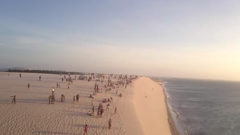 Drone-flying-over-beachgoers-tourists-on-a-sand-dune-in-Jericoacoara,-Brazil