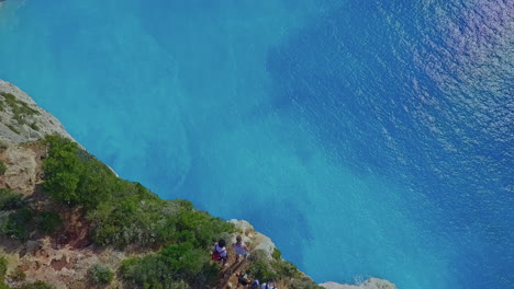 Aerial-panning-down-to-people-near-huge-cliff-over-blue-ocean-on-Greek-island