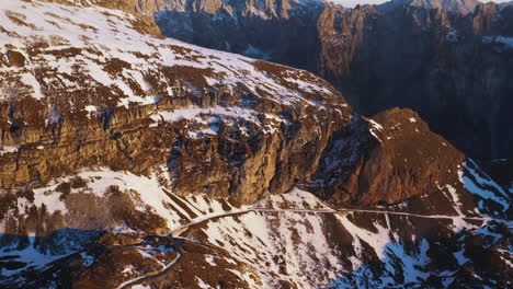 Tiro-De-Dron-Descendente-De-Una-Carretera-De-Montaña-Cubierta-De-Nieve-Y-Una-Cresta-En-La-Montaña-Mangart-En-Eslovenia