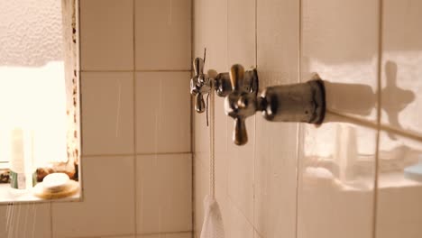 Hand-turning-bathroom-tap-making-shower-water-sprinkle-on-white-tiled-wall