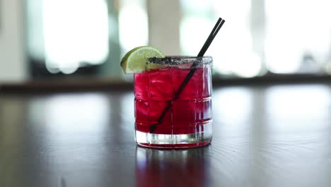 Fruchtiger-Roter-Cocktail-Mit-Limette-Und-Strohhalm-Im-Glas,-Ausgestellt-In-Einer-Bar,-Nahaufnahme