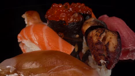Macro-view-turning-nigiri-sushi-selection-on-black-reflective-glass-background,-toro-tuna,-salmon,-lemon-fish-and-bbq-eel,-Japanese-cuisine-seafood-4K-shot