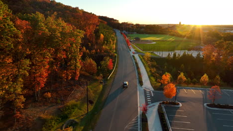 Aerial-tracking-shot-of-vehicle-driving-on-straight-road-during-autumn-fall-foliage-season-sunset