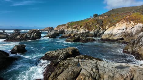 Sweeping-view-over-Blur-waves-with-white-caps-crashing-on-brown-rocks-along-pacific-coast,-Highway-1-California