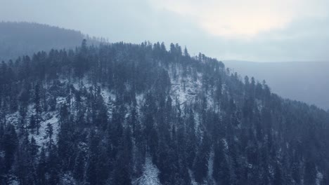 Winter-aerial-approaching-mountain-with-dark-forest-snow-covered-in-Vosges-France-4K