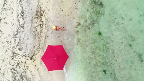 Aerial-top-view-of-woman-sunbathing-by-umbrella-on-seashore,-dolly-in