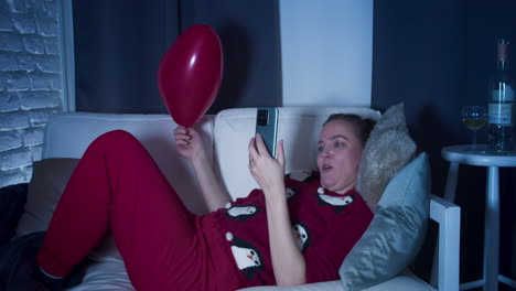 A-young-woman-in-home-clothes,-lying-on-the-couch,-watching-a-video-on-her-mobile-phone-that-makes-her-laugh-and-amazes-her