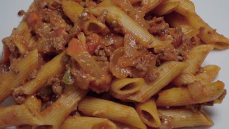 Pasta-bolognese-with-penne-noodles-on-white-plate,-Overhead-Pan-Right