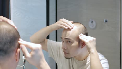POV-to-a-yong-asian-man-concerns-about-the-hair-on-his-head-from-mirror,-bald-spots-suffering-from-hair-loss