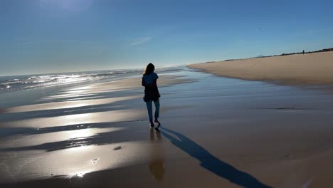 Young-woman-walking-on-a-desert-beach-under-sunset-light