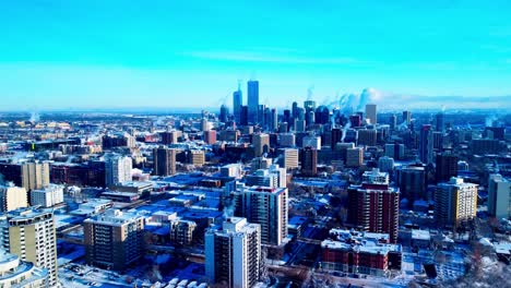 Winter-snow-covered-residential-commercial-high-rises-with-steam-coming-our-of-their-chimney's-during-an-extreme-winter-cold-weather-aerial-pan-from-downtown-West-to-South-on-clear-sunny-afternoon