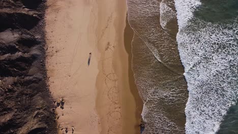 A-view-from-above-of-a-couple-walking-along-the-beach-in-Algarve,-Portugal
