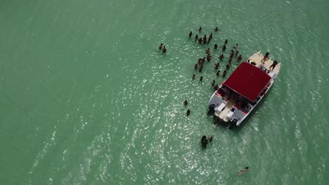 Drohne-Fliegt-über-Ein-Touristenboot-Im-Meer,-Wo-Menschen-Im-Türkisfarbenen-Meer-Stehen-Und-Das-Wasser-Genießen
