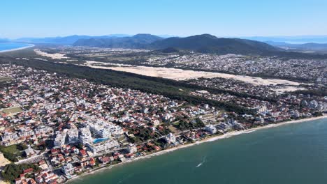 Aerial-drone-hight-scene-beach-florianópolis-seen-from-the-top-seaside-town-near-the-sea-with-mountains-dunes-horizon-buildings-urban-subdivision-on-the-coast-Ingles-beach-buildings-facing-the-sea