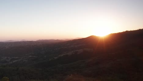 Wide-aerial-shot-of-the-sun-peeking-over-a-mountain-ridge-at-sunset