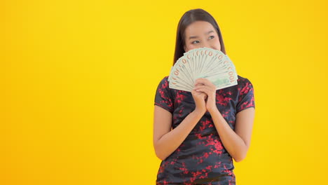 A-beautiful-Asian-woman-in-a-black-and-red-silk-dress-hides-her-face-behind-a-fan-of-hundred-dollar-bills