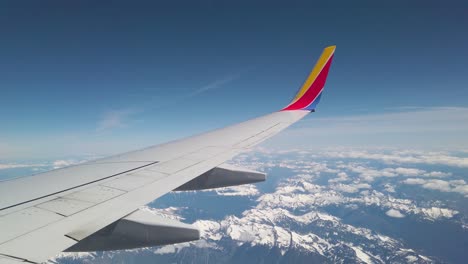 Ala-De-Avión-Volando-Alto-Sobre-Montañas-Nevadas,-Hermoso-Cielo-Azul,-Vista-Desde-La-Ventana-Del-Avión