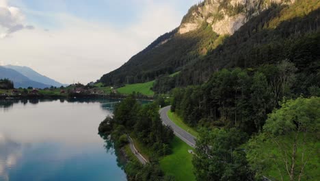 Footpath-and-driveway-on-shore-of-pristine-alpine-lake-in-Switzerland,-aerial-view