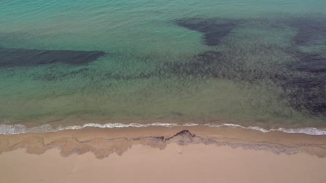 Medium-sideways-flight-right-above-sand-at-Kalogria-beach-with-view-of-ocean-spotted-dark-bottom,-Greece,-aerial