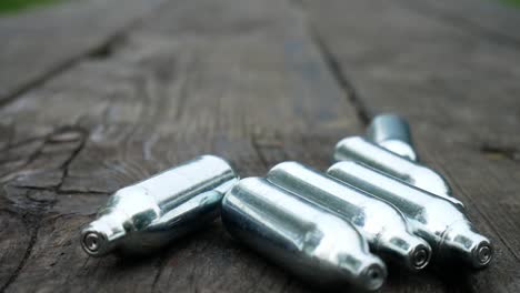 Multiple-chrome-nitrous-oxide-laughing-gas-drug-cylinders-rolling-across-wooden-park-table-closeup