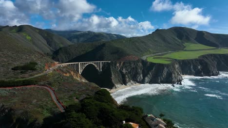 Cinematic-view-of-Bixby-Bridge-with-green-Santa-Lucia-Mountains-in-background-as-waves-crash-below,-California