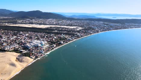 Aerial-drone-scene-beach-florianópolis-seen-from-the-top-seaside-town-near-the-sea-with-mountains-dunes-horizon-buildings-urban-subdivision-on-the-coast-Ingles-beach-and-Santinho-beach-in-sunst