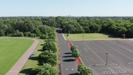 Aerial-descending-shot-above-school-parking-lot-and-athletic-track-with-Minneapolis-skyline-in-the-background