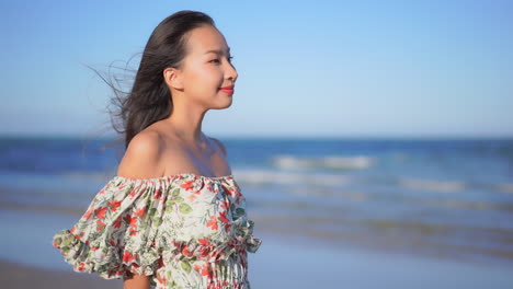 Profile-of-young-asian-female-in-summer-dress-standing-on-sandy-beach-on-light-breeze-in-hair,-slow-motion