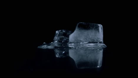Static-timelapes-shot-of-melting-cold-ice-cubes-on-a-reflective-black-surface-against-black-background