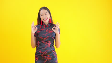 A-young-woman-dressed-in-a-black-and-red-silk-print-dress-flashes-a-big-smile-and-the-ok-sign