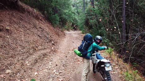Man-Climbs-Down-His-Motorcycle-In-A-Remote-Area-In-The-Forest---medium-shot