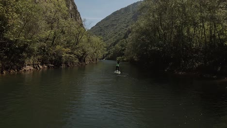 Shot-from-behind-of-a-young-girl-stand-up-paddling-along-a-canyon