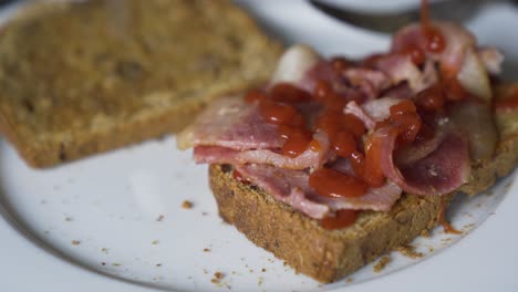 Red-sauce,-ketchup,-being-poured-over-a-bacon-sandwich-with-brown-bread