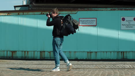 Young-male-photographer-with-backpack-stops-to-take-a-picture-of-something
