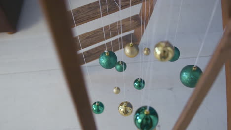 Wide-Top-Shot-of-Green-and-Golden-Christmas-Tree-Decorations-Balls,-Hanging-on-White-Thread-from-a-Wooden-Ladder-in-Slowmotion