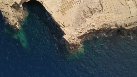 Aerial-overhead-reveal-shot-of-the-limestone-cliffs-with-salt-pans-near-canyon-Wied-il-Għasri-with-a-beautiful-clear-turquoise-water