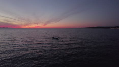 Small-recreational-fishing-boat-cruising-on-calm-dark-sea-during-twilight,-aerial