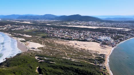 Aerial-drone-scene-beach-florianópolis-seen-from-the-top-seaside-town-near-the-sea-with-mountains-dunes-horizon-buildings-urban-subdivision-on-the-coast-Ingles-beach-and-Santinho-beach