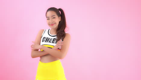 Attractive-young-Asian-woman-in-yellow-cheerleader-costume-crosses-arms-and-smiles