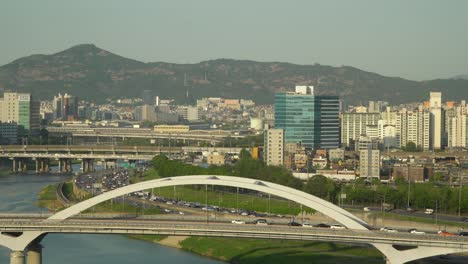 Top-view-on-Car-traffic-at-Eungbonggyo-Bridge-and-Seoul-freeway-near-Han-river-from-High-point-of-view,-many-buildings-and-Hills-on-background